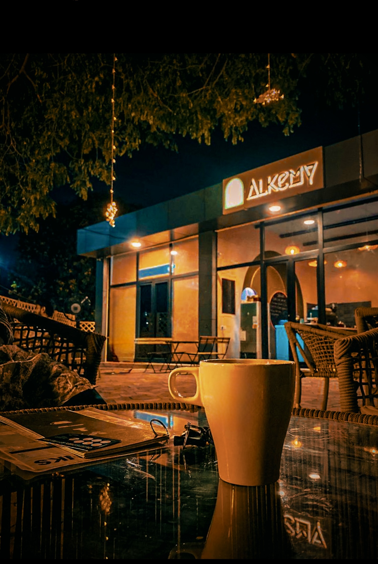 Alkemy cafe at night with glowing signage and a warm mug on the table