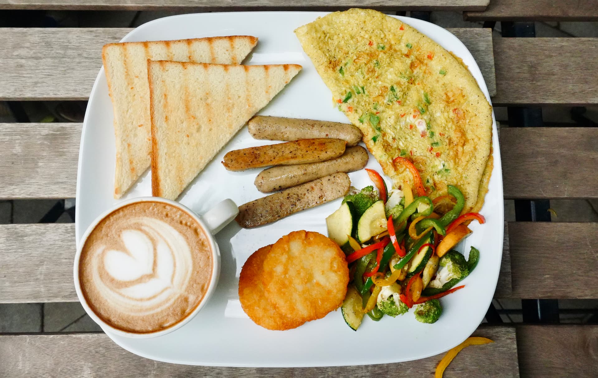 English breakfast platter with omelette, sausages, hash brown, toast and a cappuccino